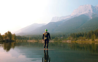 a triathlete in a full wetsuit standing in a mountain lake